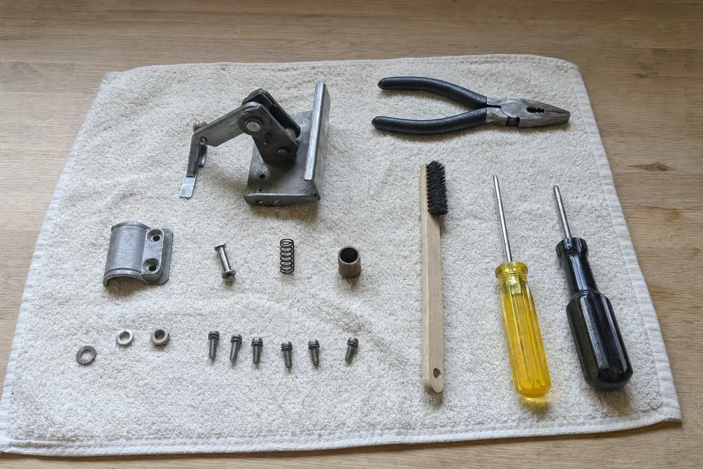 An oven door hinge taken apart on a towel — spring body, cover, pin, spring and bushing beside the screws that hold it